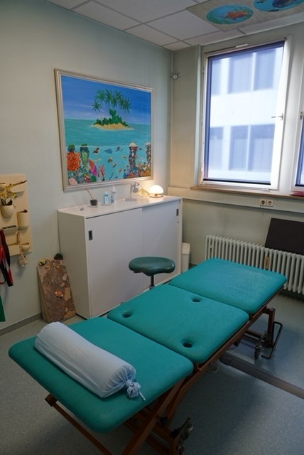 Behandlungsraum mit Therapieliege am Fenster und Inselbild